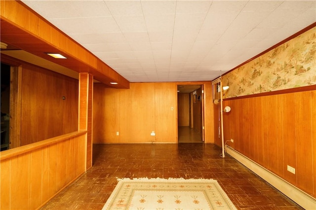 unfurnished room with a baseboard heating unit, wainscoting, wood walls, and wallpapered walls