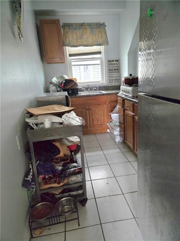 kitchen with brown cabinetry, freestanding refrigerator, a sink, and light tile patterned floors