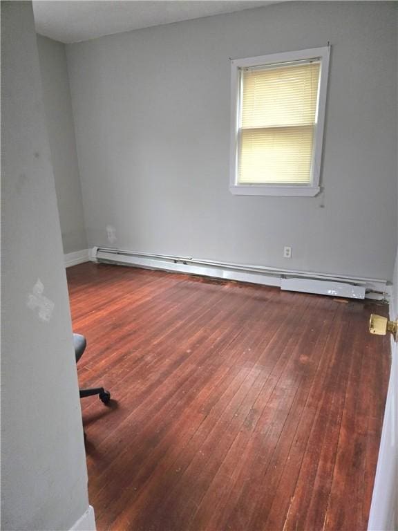 spare room featuring a baseboard heating unit and wood finished floors