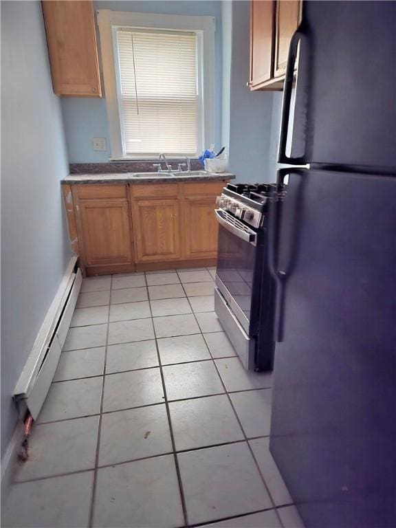 kitchen with light tile patterned floors, a baseboard radiator, a sink, freestanding refrigerator, and gas stove