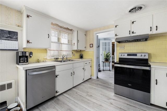 kitchen featuring wallpapered walls, white cabinets, stainless steel appliances, light countertops, and under cabinet range hood