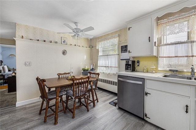 kitchen with white cabinets, radiator, light countertops, stainless steel dishwasher, and a sink