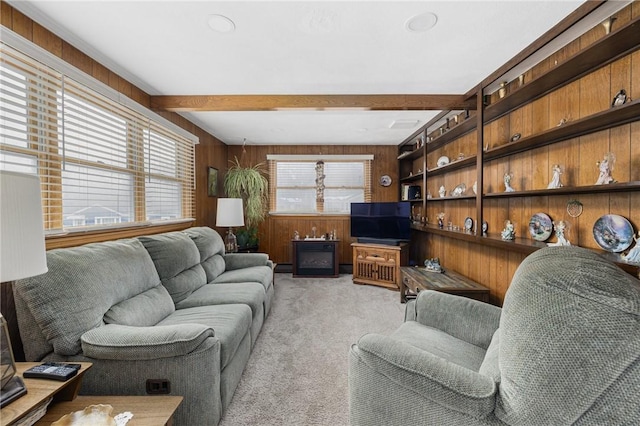 living area with wooden walls, beam ceiling, and light colored carpet