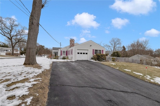 view of front facade with a garage, fence, a chimney, and aphalt driveway