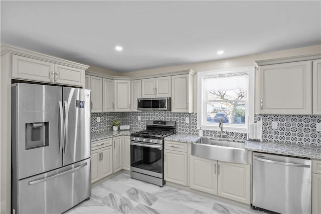 kitchen with appliances with stainless steel finishes, a sink, light stone counters, and tasteful backsplash