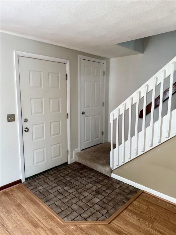 foyer entrance featuring a textured ceiling, baseboards, and dark wood-type flooring