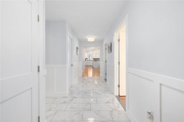 hall with a wainscoted wall, marble finish floor, and a decorative wall