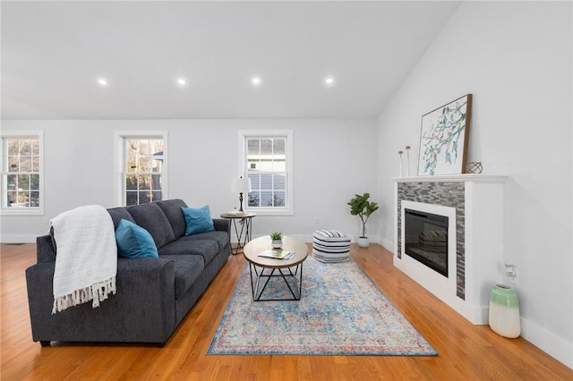 living room with light wood finished floors, recessed lighting, a glass covered fireplace, vaulted ceiling, and baseboards