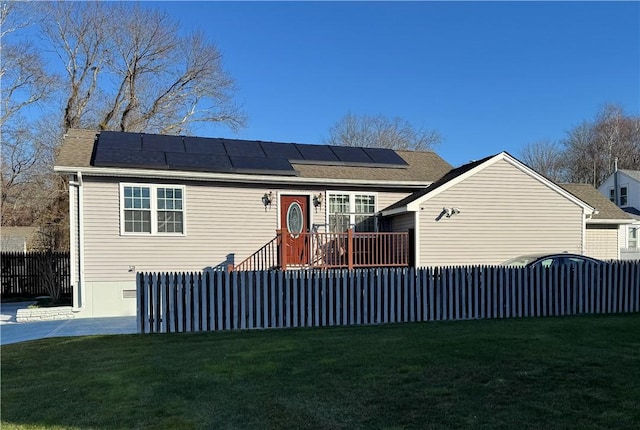 view of front facade with a front yard, fence, and roof mounted solar panels