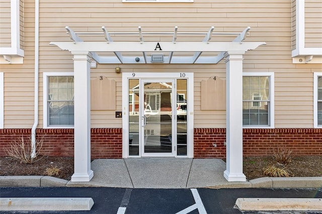 doorway to property with brick siding and a pergola