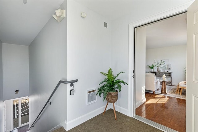 corridor with an upstairs landing, heating unit, baseboards, and wood finished floors