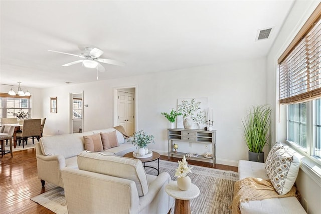 living room with visible vents, ceiling fan with notable chandelier, baseboards, and wood finished floors