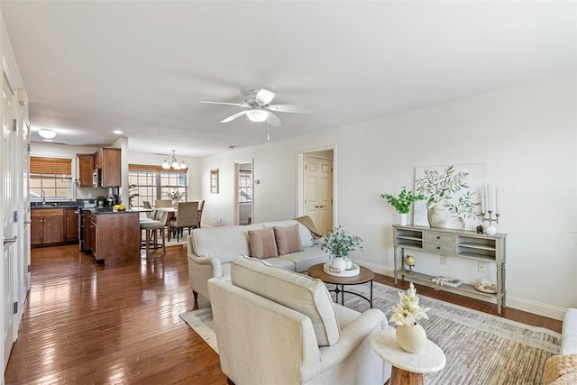 living room with dark wood-style floors, ceiling fan with notable chandelier, and baseboards