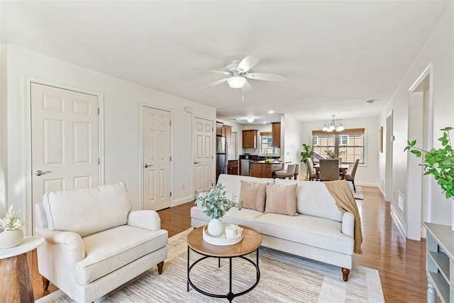 living area with baseboards, ceiling fan with notable chandelier, visible vents, and light wood finished floors