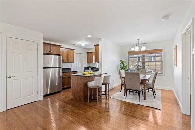 kitchen featuring a breakfast bar area, wood finished floors, baseboards, freestanding refrigerator, and a chandelier