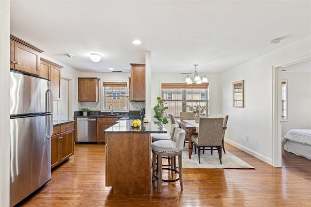 kitchen with baseboards, a kitchen bar, wood finished floors, stainless steel appliances, and a sink