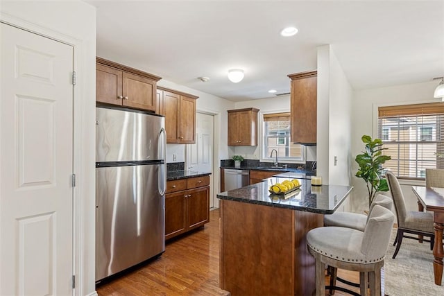 kitchen with a kitchen bar, a sink, wood finished floors, stainless steel appliances, and dark stone counters