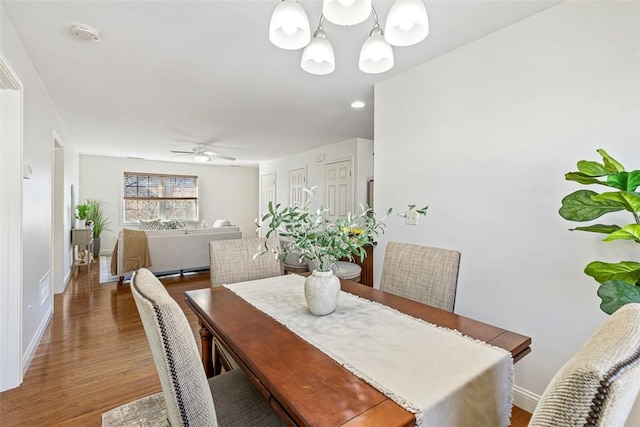 dining room featuring ceiling fan with notable chandelier, wood finished floors, and baseboards