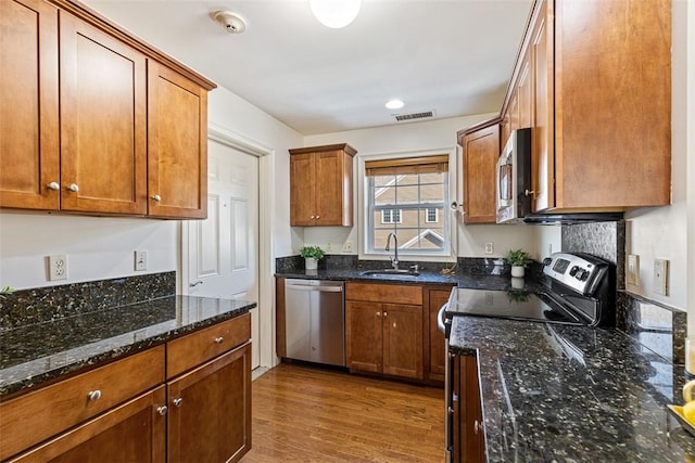 kitchen featuring visible vents, a sink, dark stone countertops, appliances with stainless steel finishes, and dark wood-style flooring