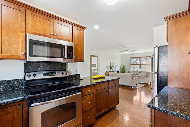 kitchen featuring dark stone countertops, wood finished floors, open floor plan, stainless steel appliances, and brown cabinetry