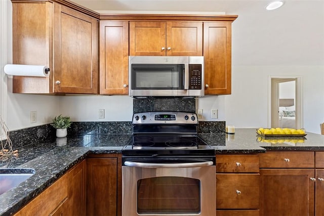 kitchen with dark stone counters, brown cabinetry, and appliances with stainless steel finishes