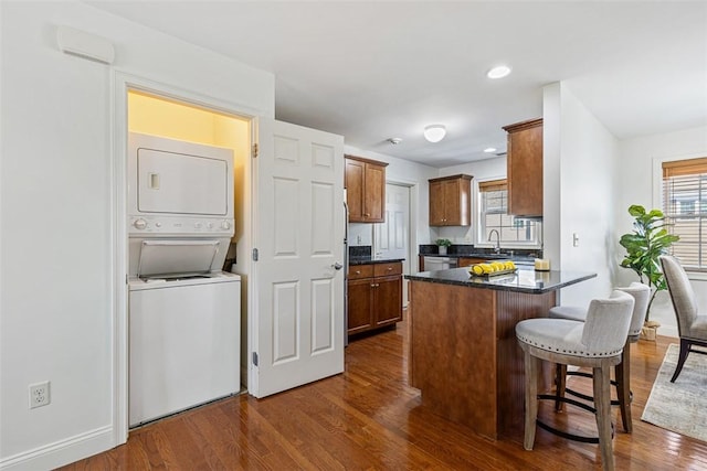 kitchen with dark wood-type flooring, a kitchen bar, a peninsula, stacked washing maching and dryer, and a sink