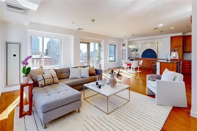 living area with recessed lighting, light wood-type flooring, visible vents, and a city view