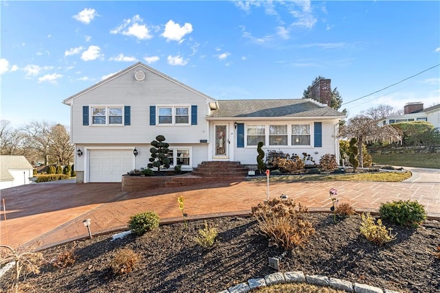 tri-level home featuring entry steps, driveway, a chimney, and a garage