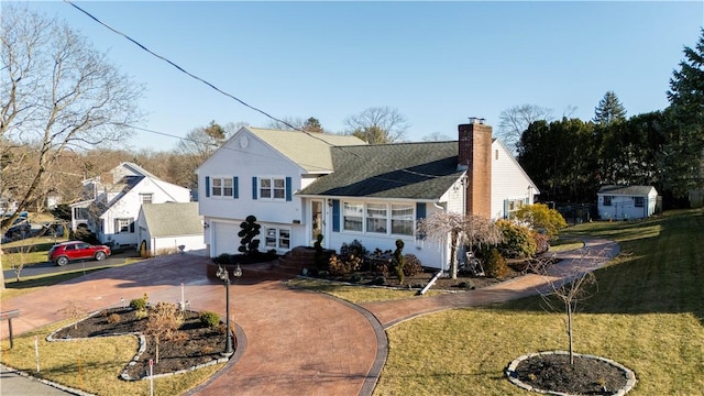 view of front of property with an attached garage, driveway, a chimney, and a front yard