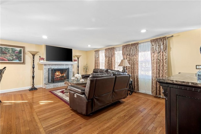 living room featuring baseboards, recessed lighting, a tiled fireplace, and light wood-style floors