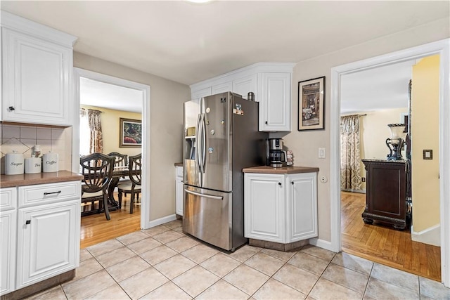 kitchen with white cabinets, dark countertops, stainless steel refrigerator with ice dispenser, and backsplash