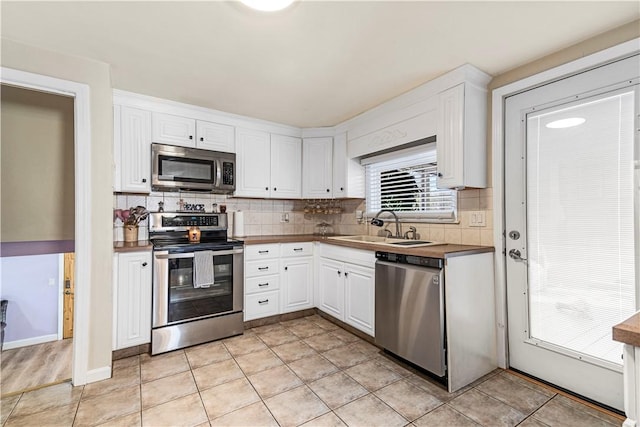 kitchen with light tile patterned floors, stainless steel appliances, a sink, white cabinets, and tasteful backsplash