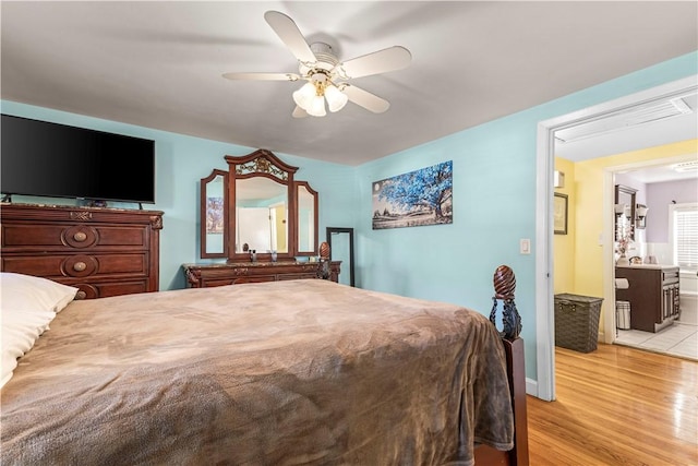 bedroom with ensuite bathroom, light wood finished floors, and a ceiling fan