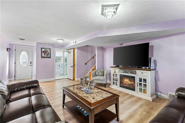 living room featuring light wood-style flooring, stairway, baseboards, and a glass covered fireplace