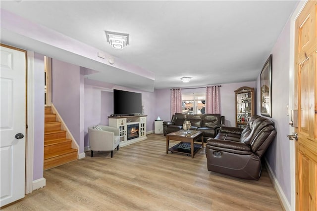 living area featuring light wood-type flooring, a lit fireplace, stairway, and baseboards