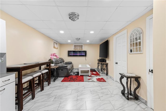 living area with recessed lighting, marble finish floor, a paneled ceiling, and baseboards