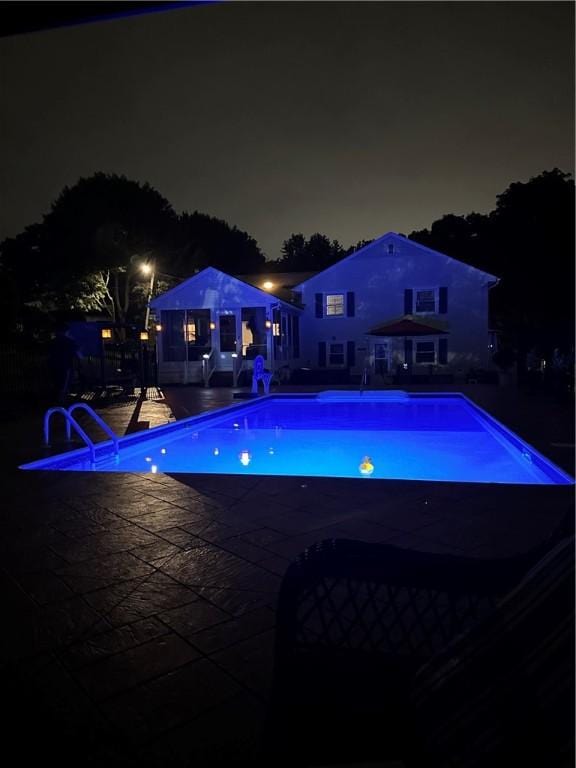 pool at night with an outdoor pool and a patio