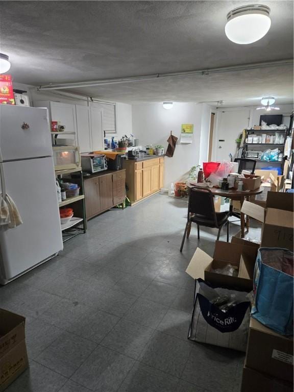 basement featuring dark floors, a textured ceiling, and freestanding refrigerator