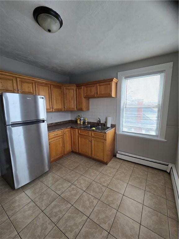 kitchen with a baseboard heating unit, a sink, freestanding refrigerator, brown cabinets, and dark countertops