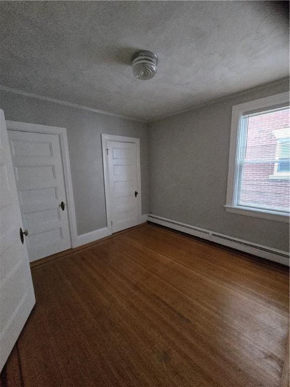 unfurnished bedroom with a baseboard heating unit, dark wood-type flooring, a textured ceiling, and baseboards