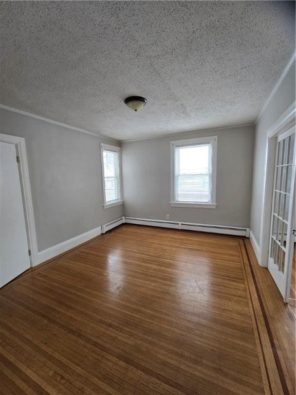 spare room featuring crown molding, a textured ceiling, baseboard heating, and wood finished floors