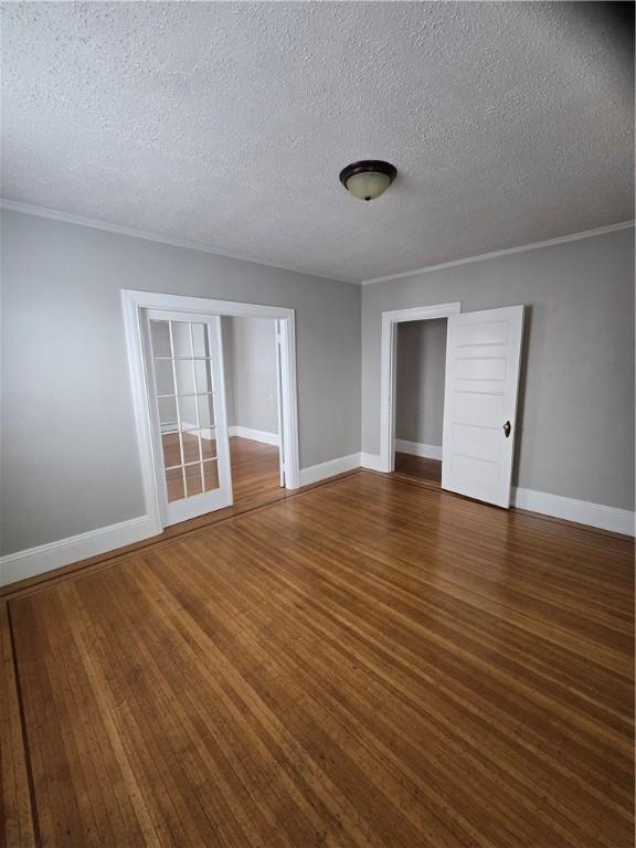 spare room featuring a textured ceiling, baseboards, dark wood-type flooring, and ornamental molding