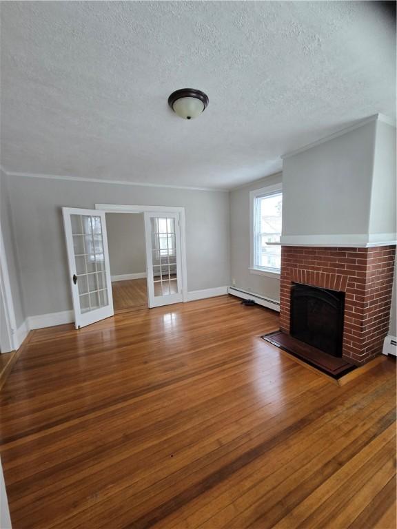 unfurnished living room with french doors, a baseboard heating unit, a brick fireplace, wood finished floors, and baseboards