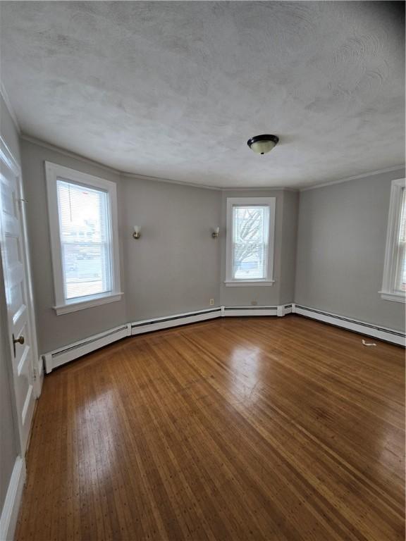 unfurnished room with a textured ceiling, ornamental molding, baseboard heating, and wood finished floors