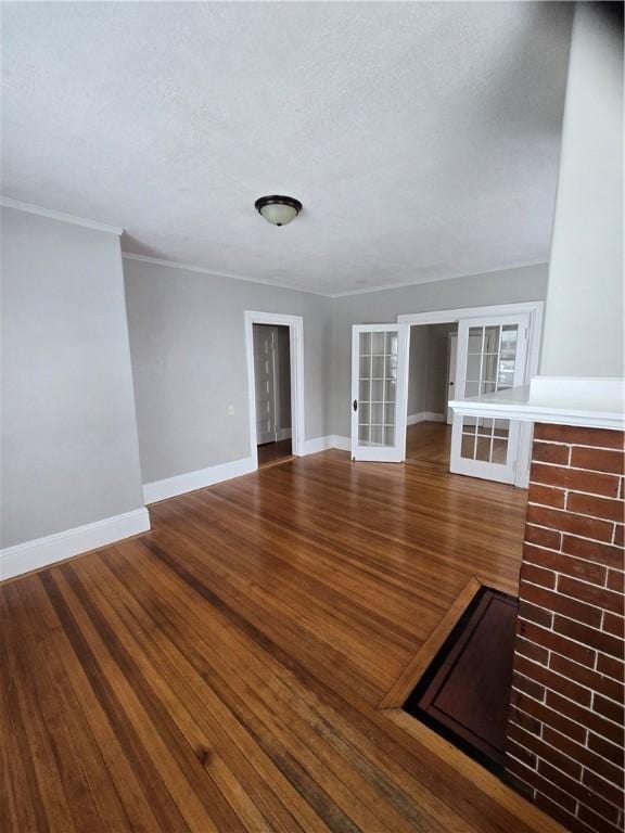 unfurnished living room with crown molding, a textured ceiling, baseboards, and wood finished floors