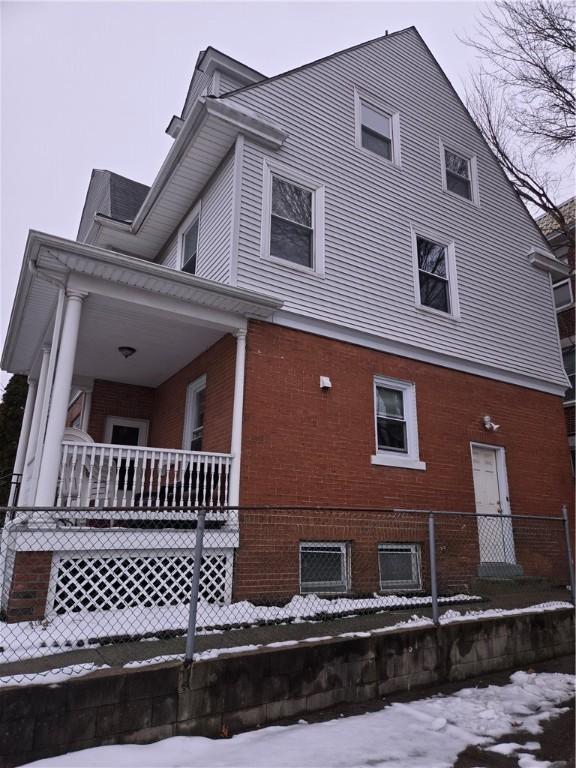 view of snowy exterior with a porch and brick siding