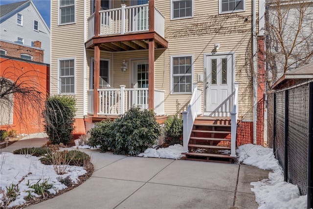 snow covered property entrance with a balcony and fence