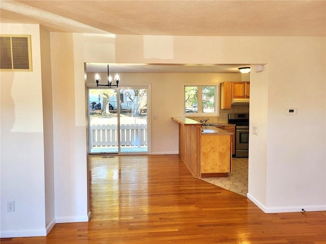 kitchen featuring visible vents, baseboards, light wood-style flooring, under cabinet range hood, and gas stove