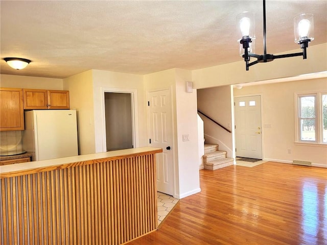 kitchen with a textured ceiling, visible vents, baseboards, freestanding refrigerator, and light wood finished floors