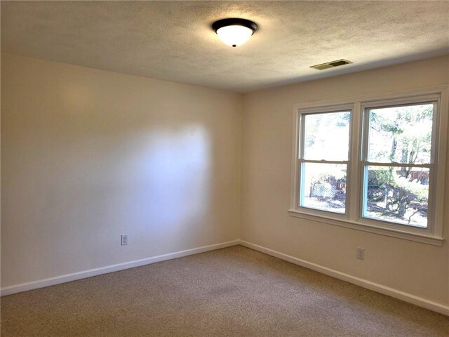 empty room featuring baseboards, a textured ceiling, visible vents, and light colored carpet